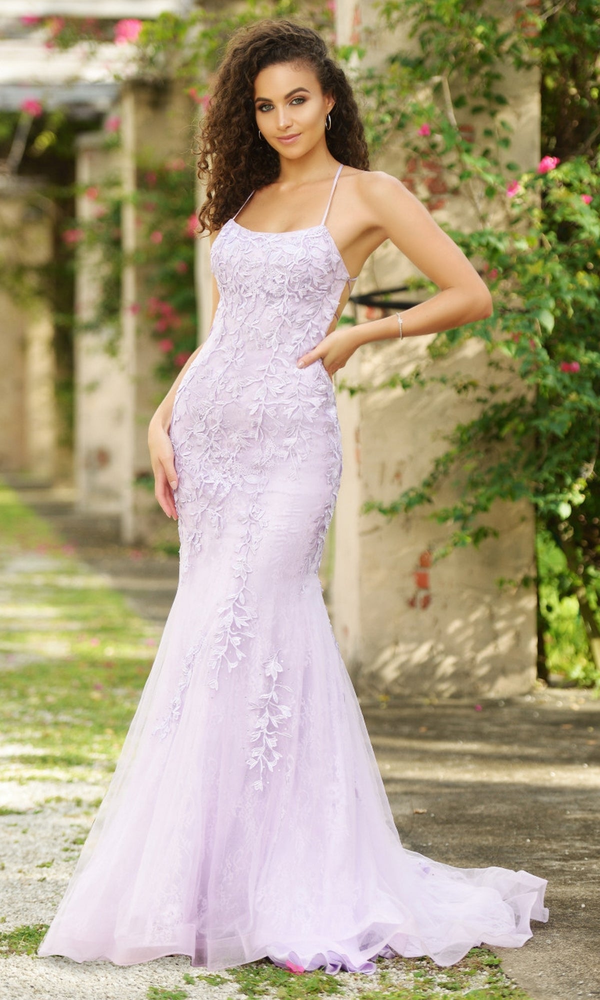 A woman stands outdoors in the Beaded Lace Long Prom Dress Dutchess, a fitted, floor-length gown featuring a mermaid silhouette and thin straps. She poses confidently with one hand on her hip.